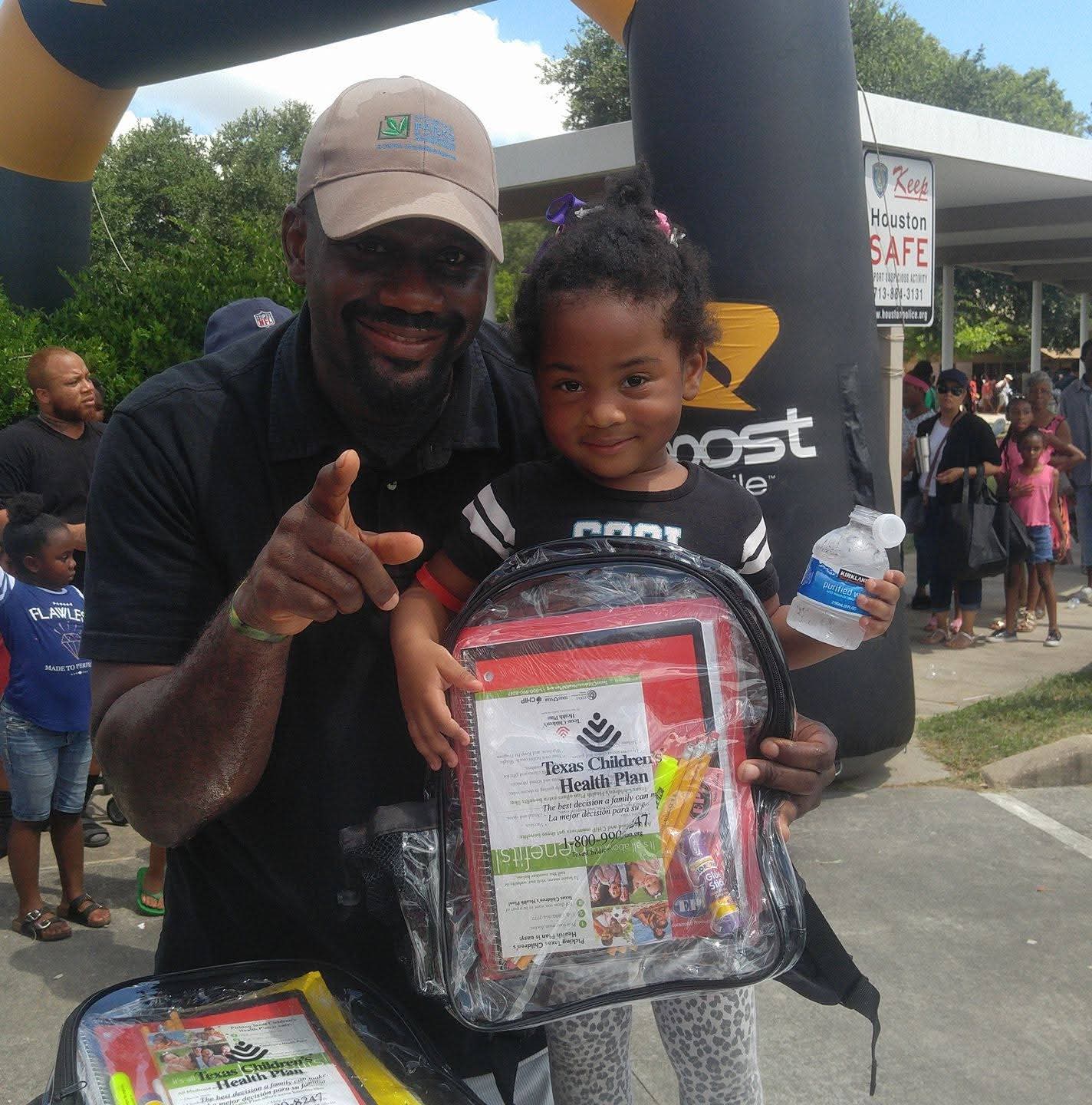 Jerry Davis handing a school supply backpack to a young student